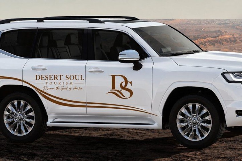 A white SUV with 'Desert Soul Tourism' branding and a desert landscape in the background. 2