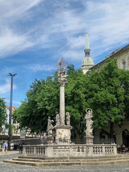 Un monumento histórico con estatuas, una fuente e iglesia con aguja verde al fondo. 3