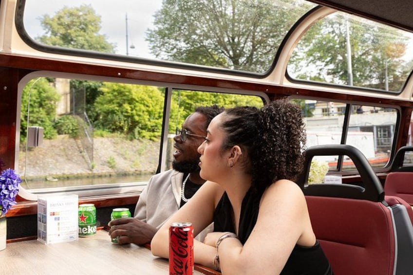 A person sitting at a table inside a vehicle with a window view of greenery and buildings. 4