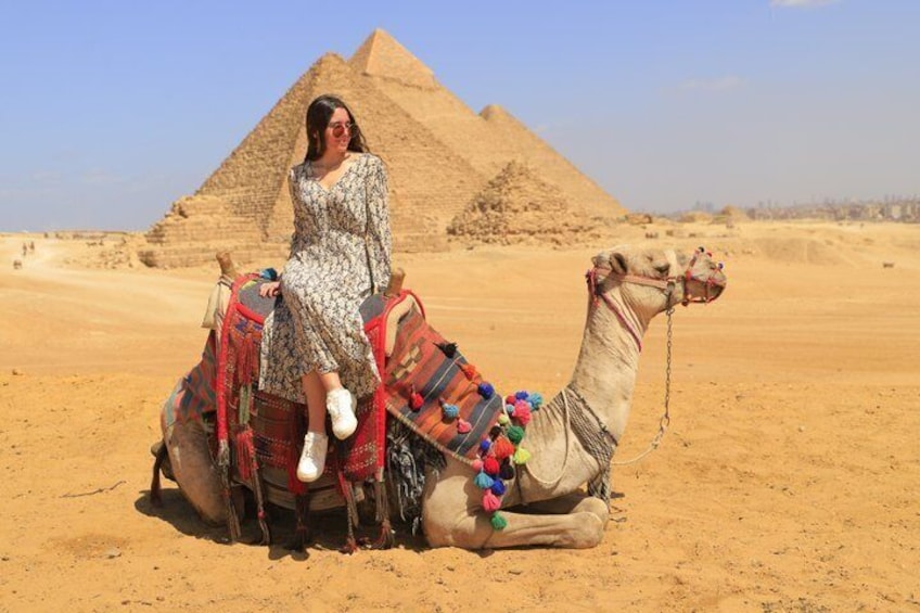A person riding a camel in a desert with pyramids in the background. 5