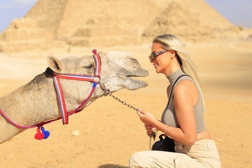 A person interacting with a camel in a desert setting with pyramids in the background. 2
