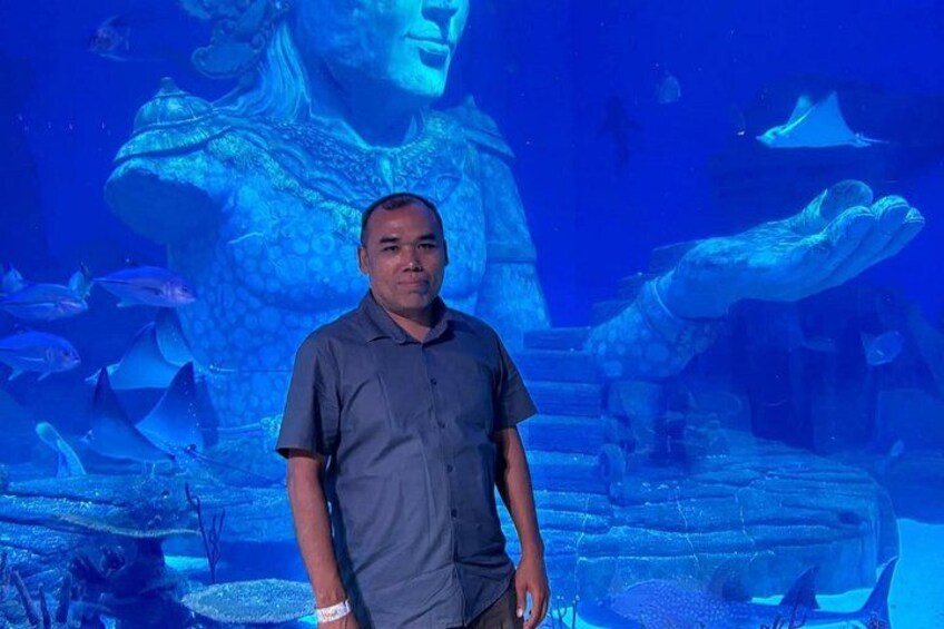 Un hombre de pie frente a un acuario con un gran mural de una sirena y varios peces. 5