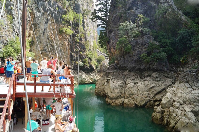A group of people on a wooden boat in a rocky canyon with a clear turquoise river. 2