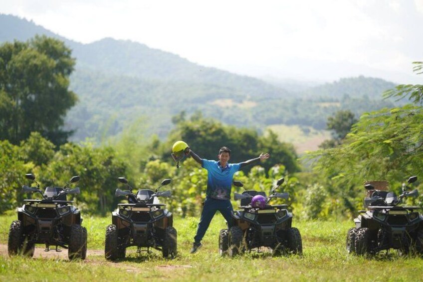 A person with arms outstretched in a grassy field with four quad bikes. 1