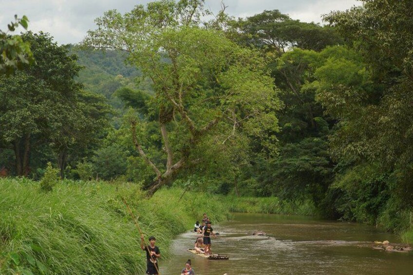 A river with people on a raft, surrounded by dense greenery and trees. 2