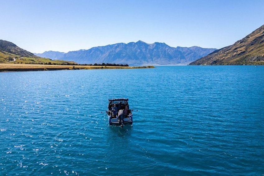 A vehicle on a calm lake with mountains in the background. 2