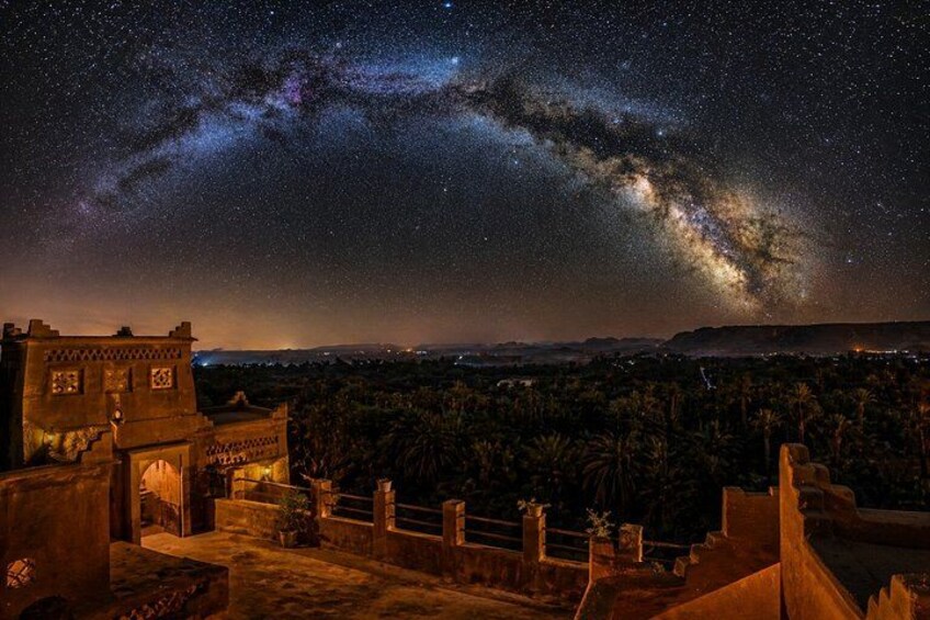 A night sky with stars and the Milky Way over a cityscape with buildings and palm trees. 2