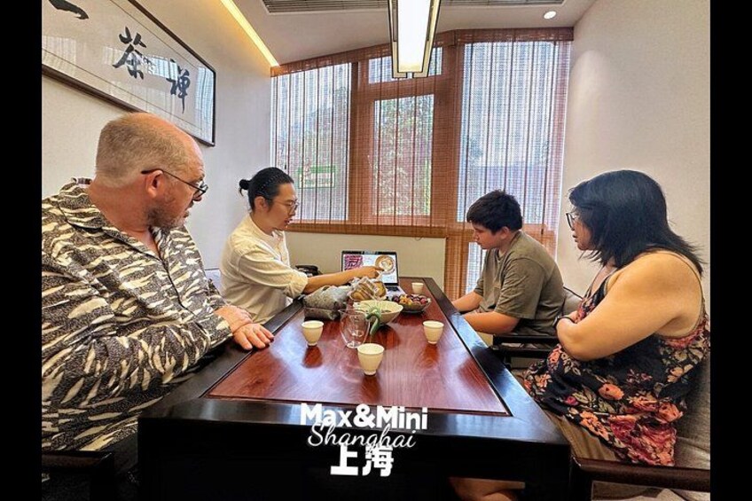A group of people seated around a wooden table in a room with large windows and traditional decor. 4