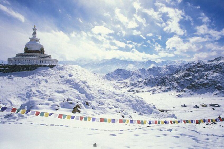A snow-covered mountain landscape with a large white building, possibly a temple, and colorful prayer flags. 4