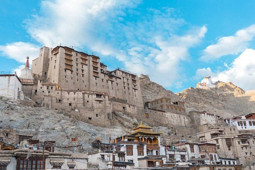 A large, multi-story building with a traditional architectural style, situated on a rocky hillside with a clear sky above. 3