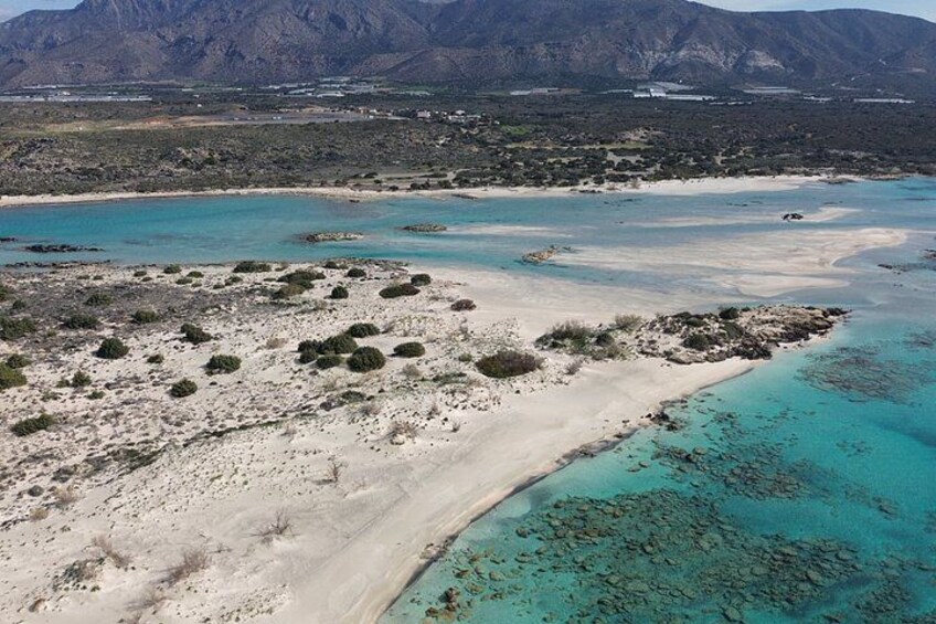 A coastal landscape with a sandy beach, turquoise waters, and distant mountains. 4