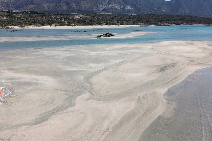 A beach with sand patterns, a body of water, and mountains in the background. 3