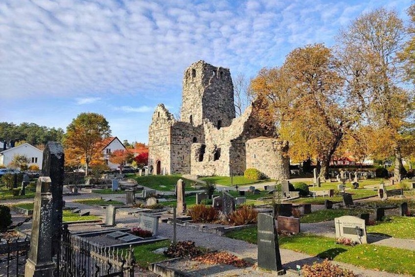 A historic stone building with a tower, surrounded by a cemetery with gravestones and trees with autumn foliage. 2