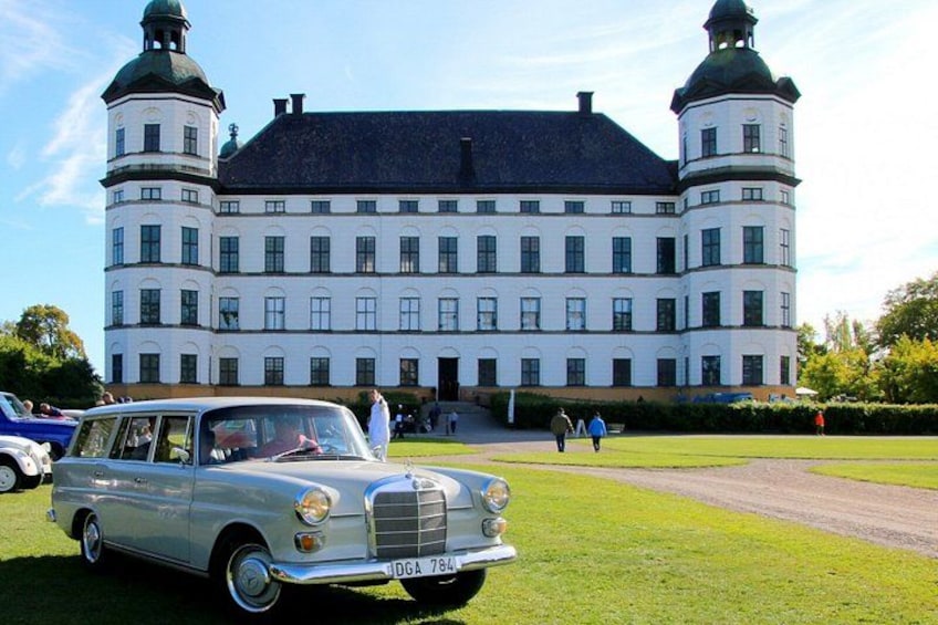 A classic white car parked in front of a large white building with two green domed towers. 5