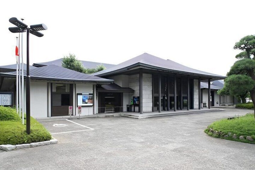 A modern building with a covered entrance, a parking lot, and a small garden area. 2
