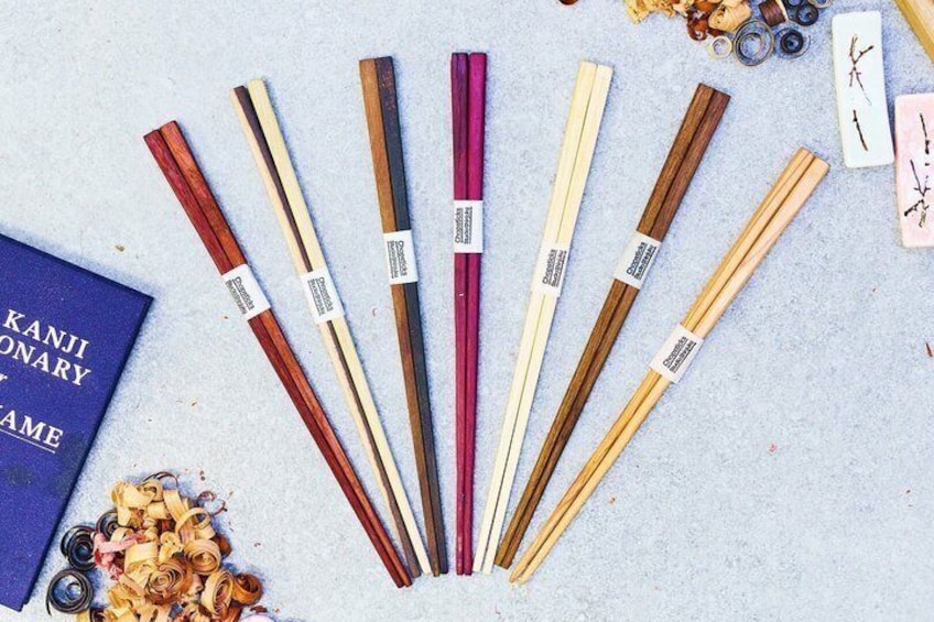 A variety of chopsticks with different colors and materials, arranged on a surface with a book and some decorative items. 1