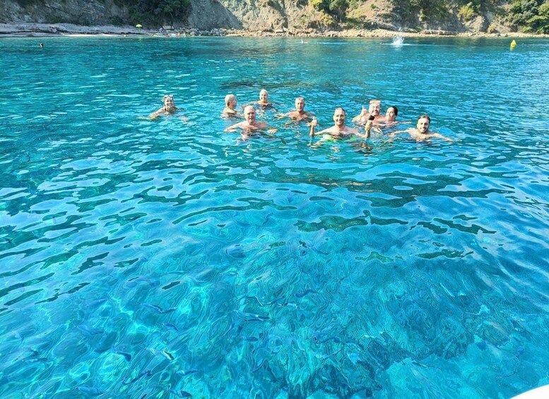 A group of people swimming in clear blue water with a rocky coastline in the background. 2