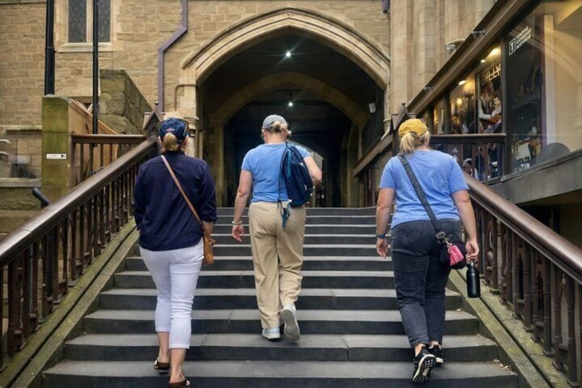 Three people walking up a set of stone steps towards an arched entrance. 4