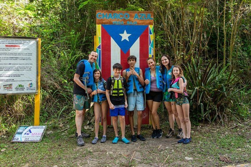 A group of people standing in front of a colorful sign with a star and stripes, surrounded by greenery. 4