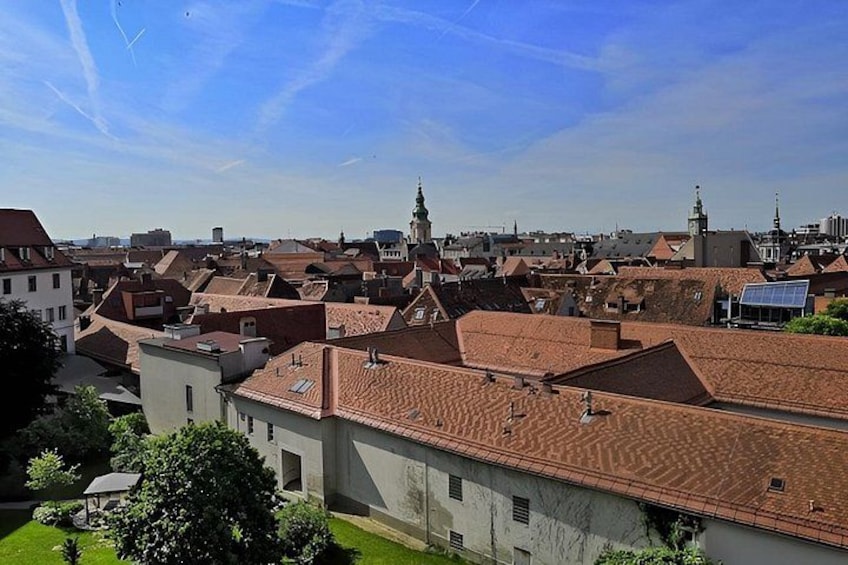 A cityscape with red-tiled roofs, a prominent church tower, and a clear blue sky. 4