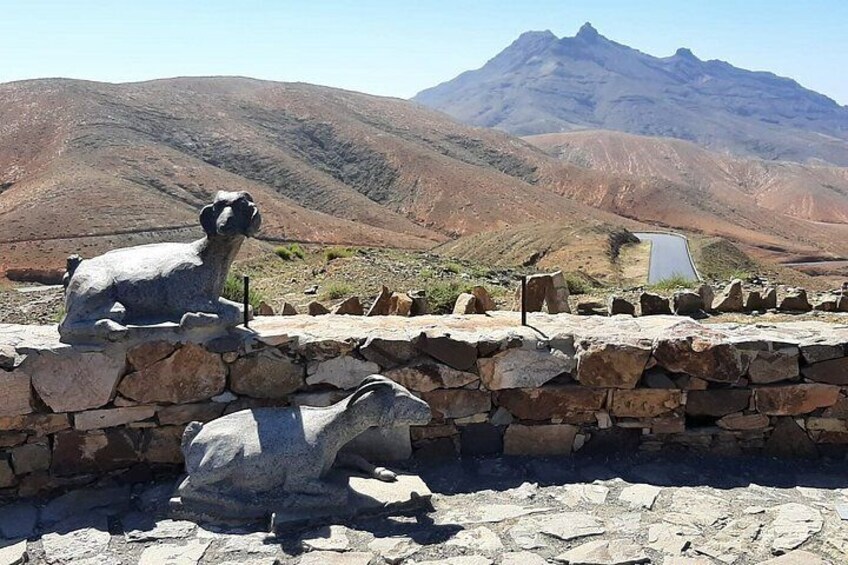 A stone sculpture of a camel and a stone wall with a mountainous landscape in the background. 5