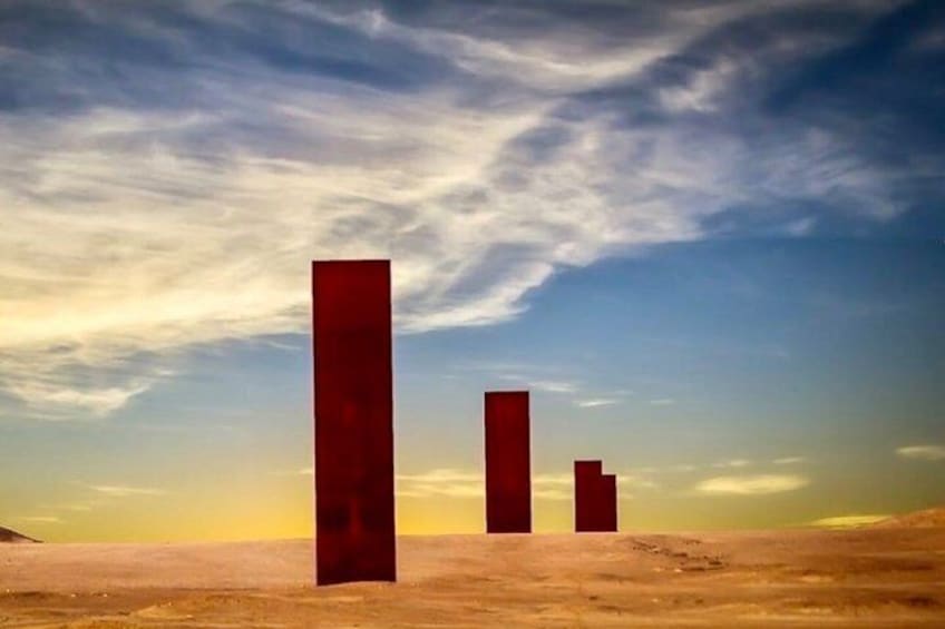 Three vertical red structures in a desert landscape with a clear sky. 1