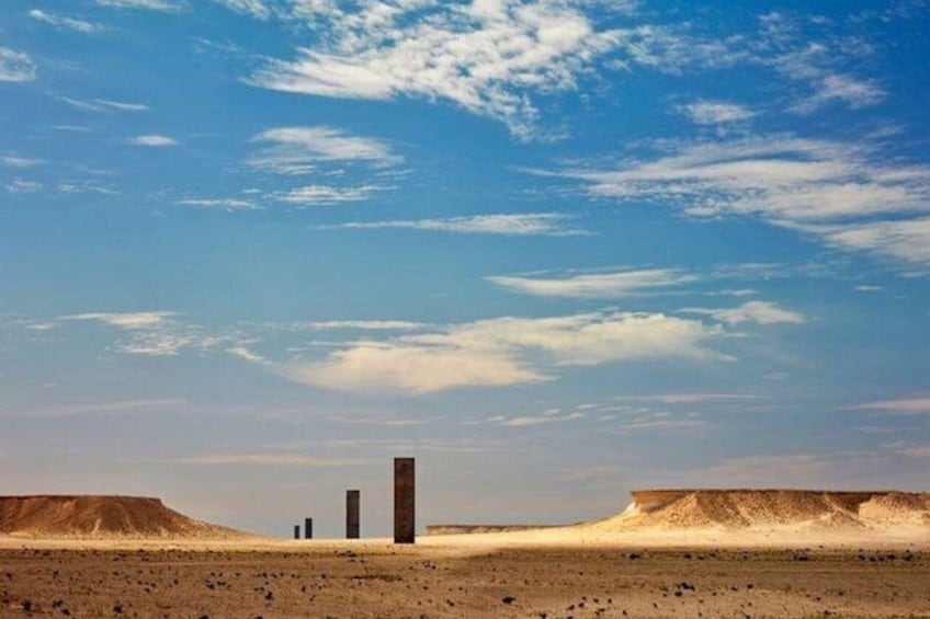 A desert landscape with three tall, dark structures in the distance. 3