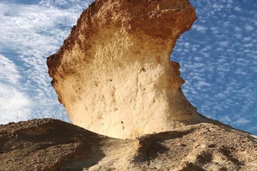 A large rock formation with a distinct overhang against a clear sky. 4