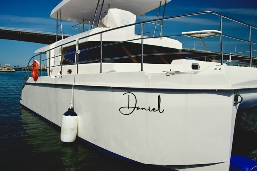 A white yacht named 'Daniel' docked at a marina with a bridge in the background. 4