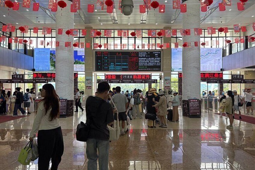 A busy airport terminal with people walking, check-in counters, and red lanterns hanging from the ceiling. 4