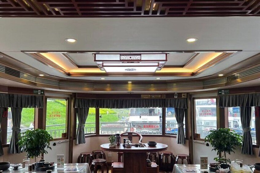 A restaurant with a round table, chairs, potted plants, and large windows. 3