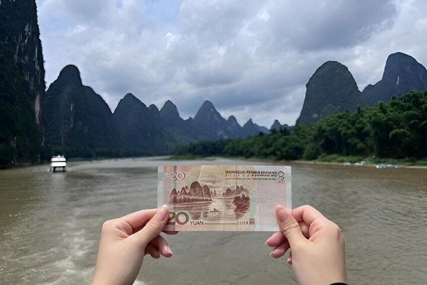 Hands holding a 20 yuan note with a mountainous landscape and a boat in the background. 5