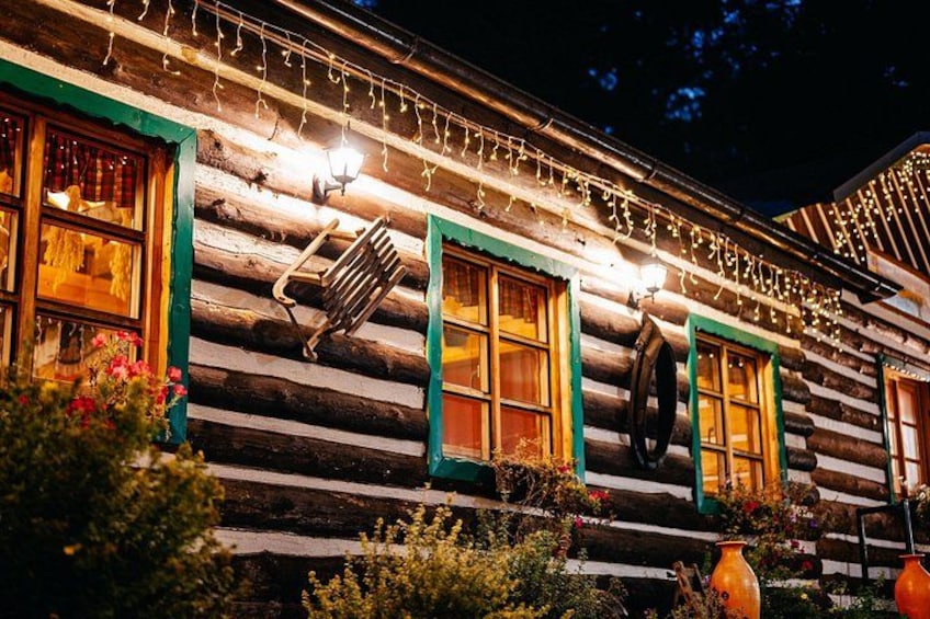 A log cabin with green trim, string lights, and a metal bench. 2