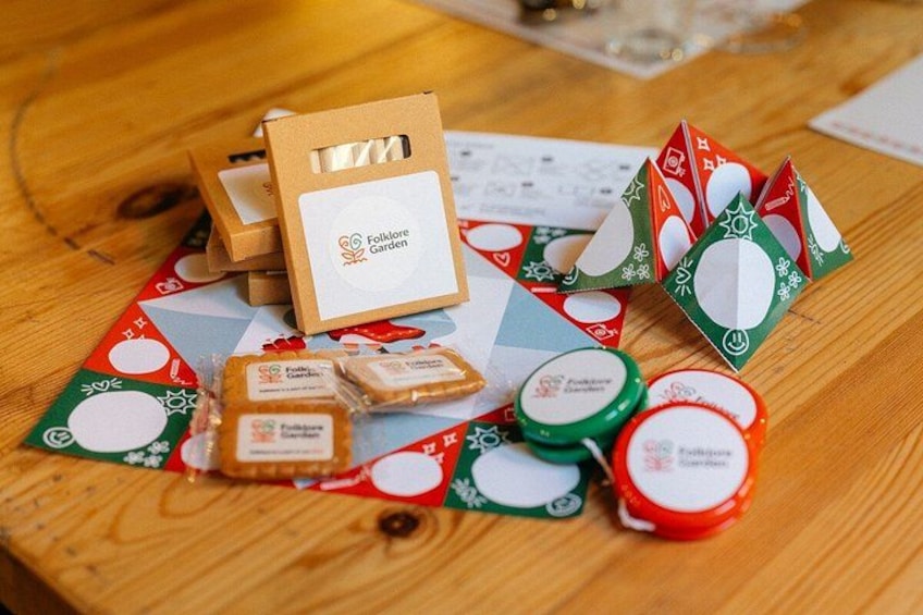 A wooden table with a Folklore Garden card, a red and green paper craft, and some small jars. 4