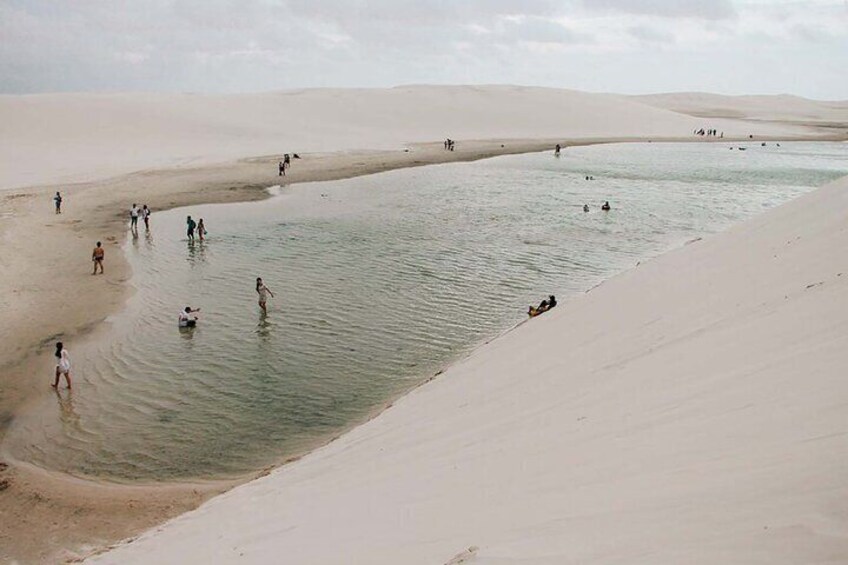 A desert landscape with a large body of water, people swimming, and sand dunes. 2