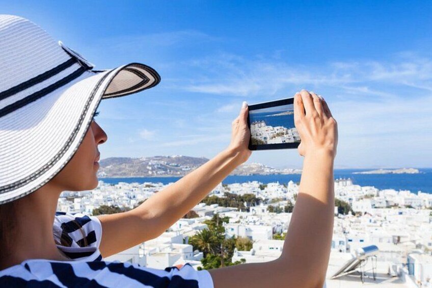 A person taking a photo of a coastal town with white buildings and a clear blue sky. 3