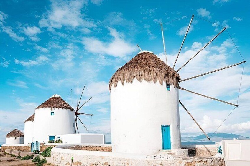 White windmills with thatched roofs and blue doors, set against a clear blue sky. 3