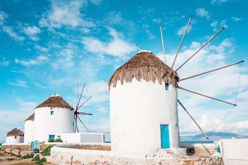 White windmills with thatched roofs and blue doors, set against a clear blue sky. 3