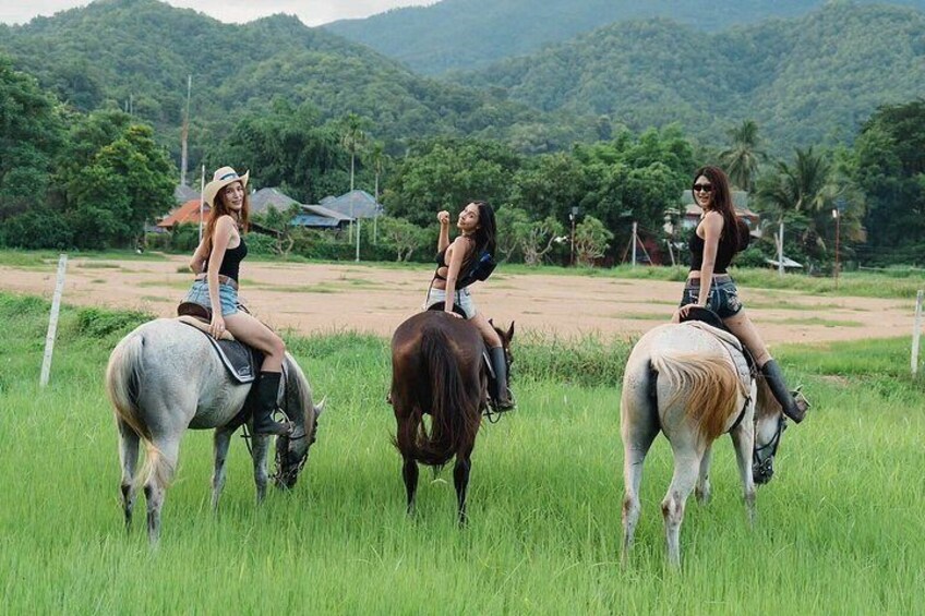 Three women riding horses in a grassy field with a mountainous background. 5
