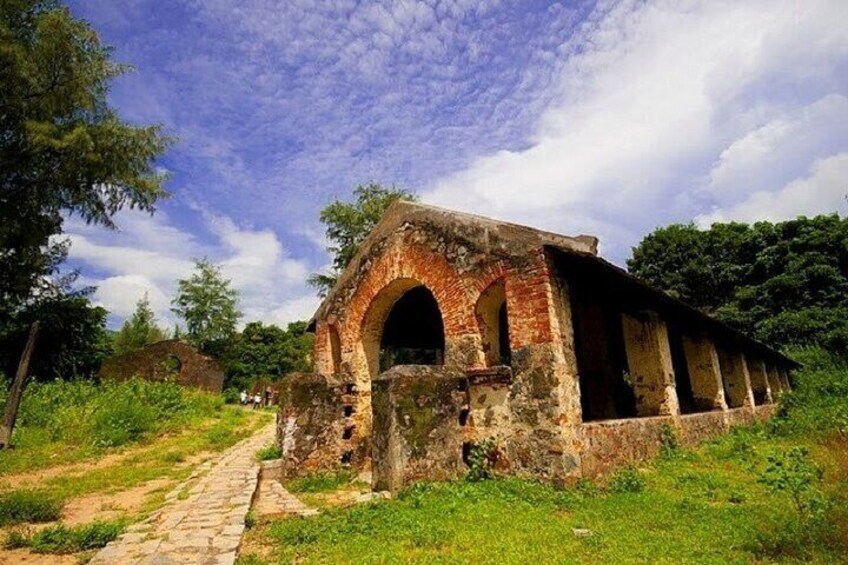 An ancient brick structure with a large archway, surrounded by greenery and a clear sky. 5