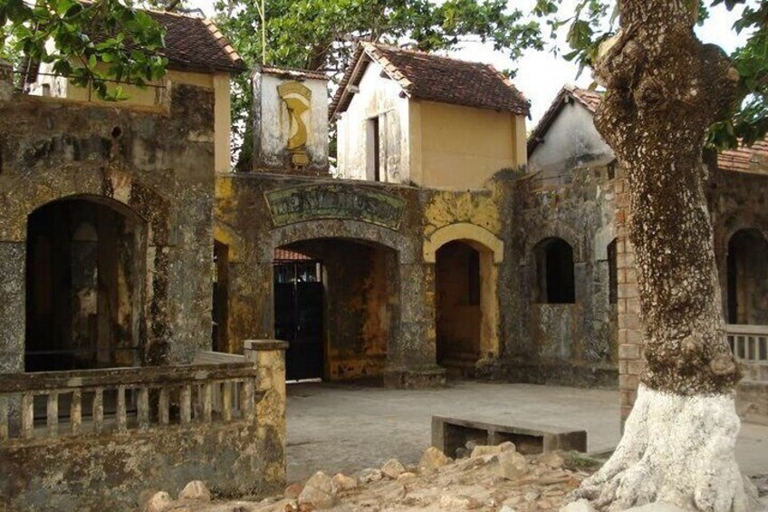 An old courtyard with stone walls, a central archway, and a tree. 4