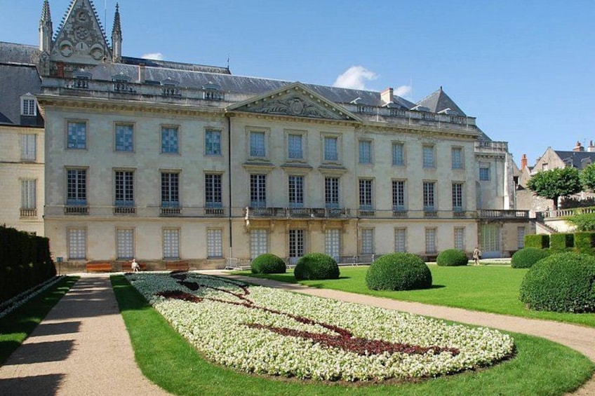 A large, historic building with a symmetrical facade, a formal garden with geometric hedges, and a clear sky. 2