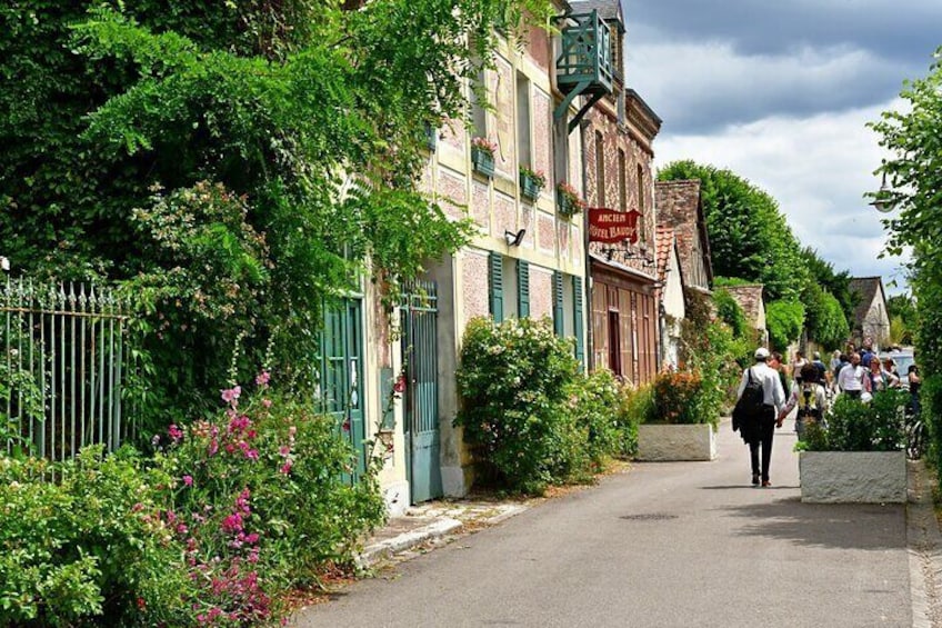 A narrow street lined with buildings, a person walking, and greenery. 5
