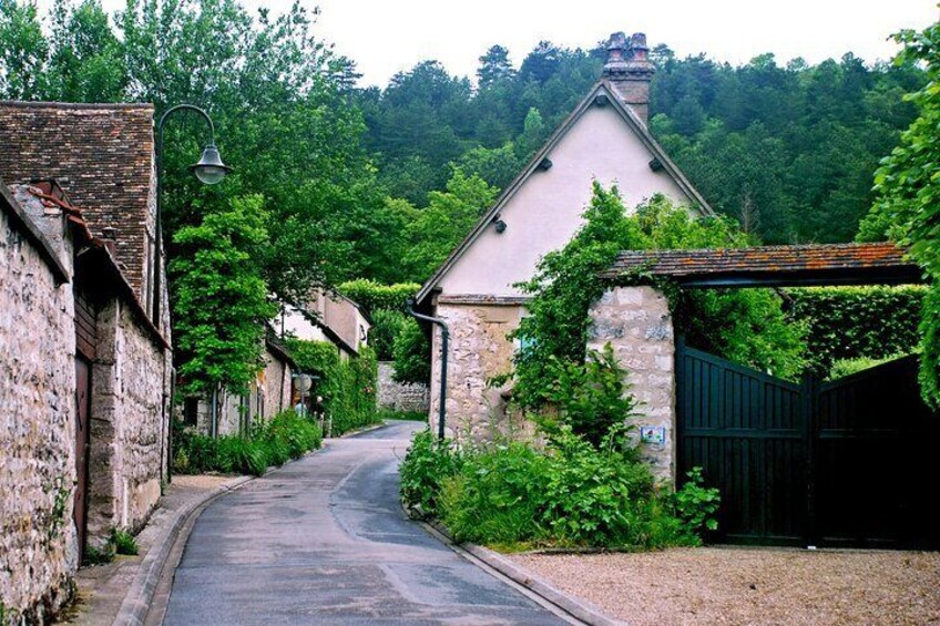 A narrow village street lined with stone buildings, a green gate, and lush greenery. 3