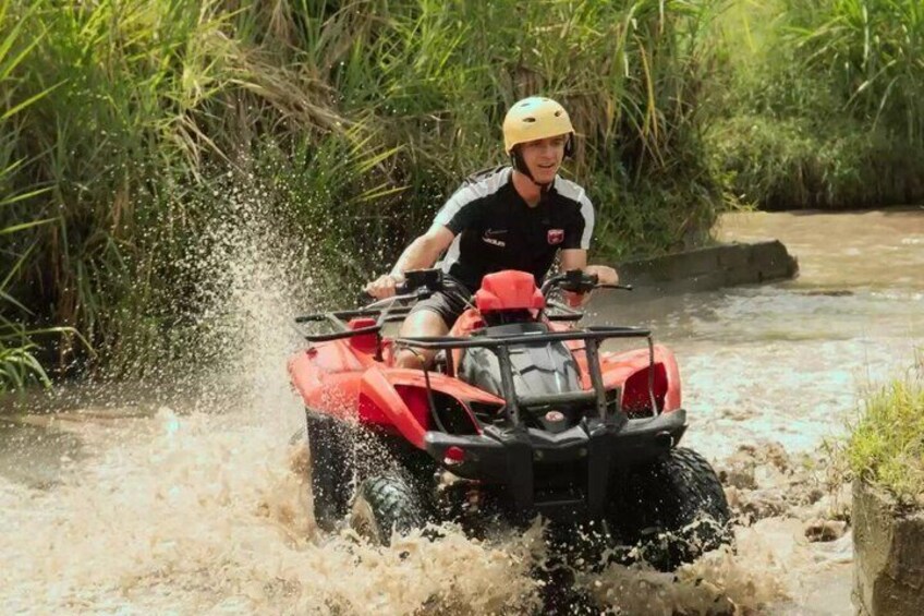 A person riding a red ATV through a shallow water crossing. 3