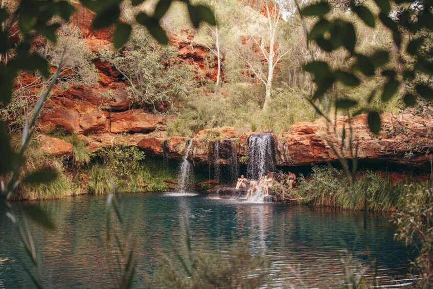 A waterfall in a natural setting with red rock formations and greenery. 1