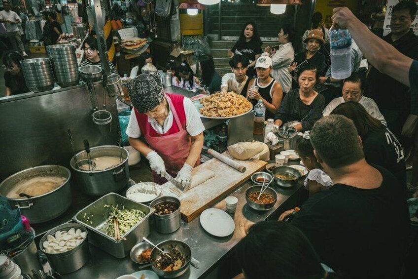 A bustling food stall with a cook preparing food, surrounded by various cooking utensils and ingredients. 1