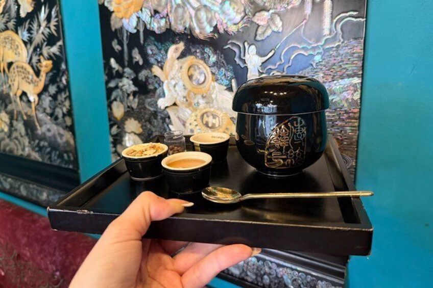 A hand holding a tray with four cups and a spoon, set against a backdrop of a colorful mural. 2