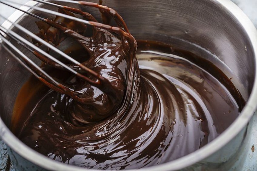 A metallic mixing bowl with melted chocolate being stirred. 3