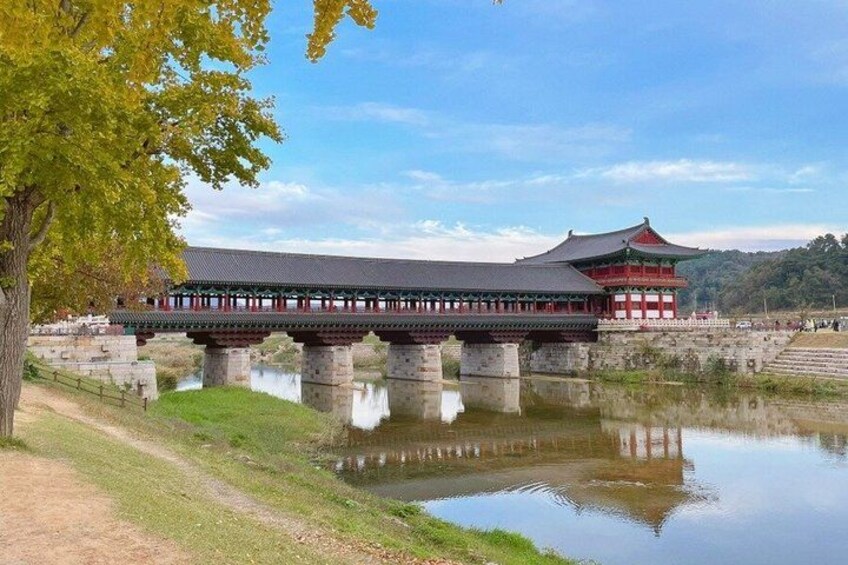 A traditional Korean bridge over a calm river, with a red building in the background. 2